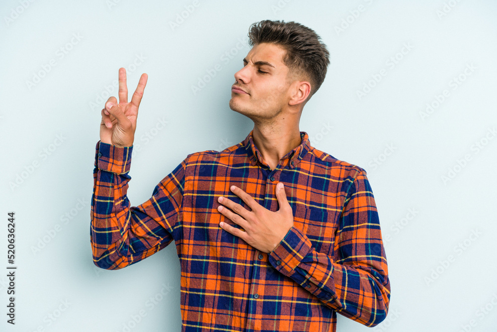 Young caucasian man isolated on blue background taking an oath, putting hand on chest. Young caucasian man isolated on blue background taking an oath, putting hand on chest.