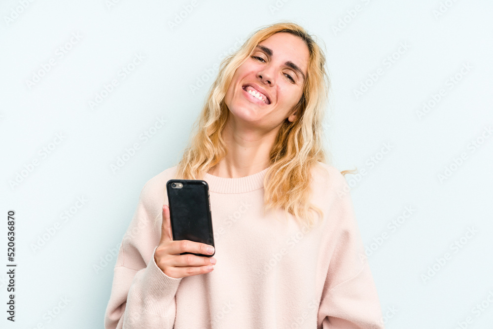 Young caucasian woman holding mobile phone isolated on blue background happy, smiling and cheerful. Young caucasian woman holding mobile phone isolated on blue background happy, smiling and cheerful.
