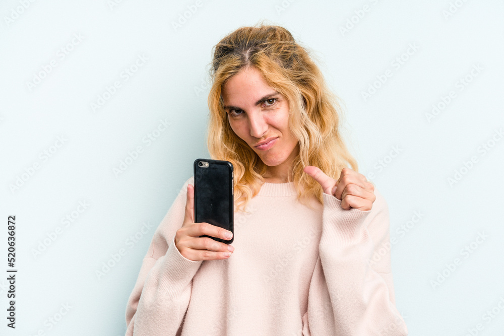 Young caucasian woman holding mobile phone isolated on blue background feels proud and self confident, example to follow. Young caucasian woman holding mobile phone isolated on blue background feels proud and self confident, example to follow.