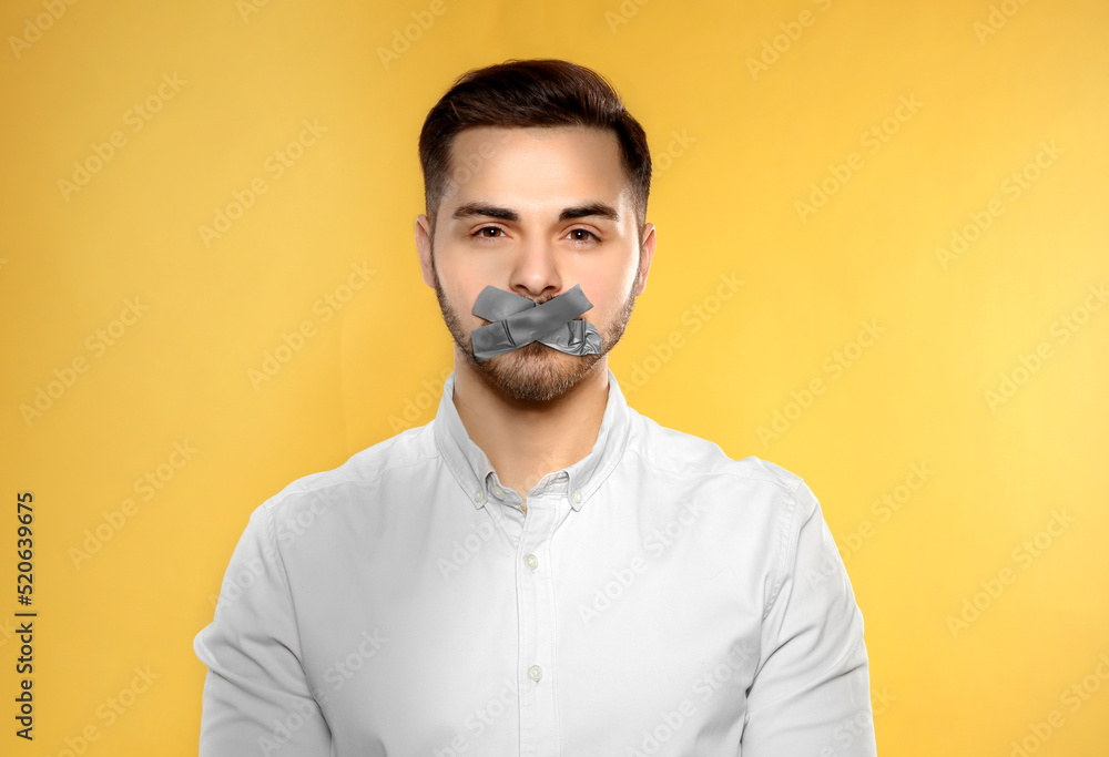 Obraz premium Man with taped mouth on yellow background. Speech censorship