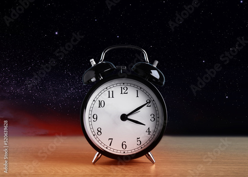 Alarm clock on wooden table against night sky with stars. Insomnia
