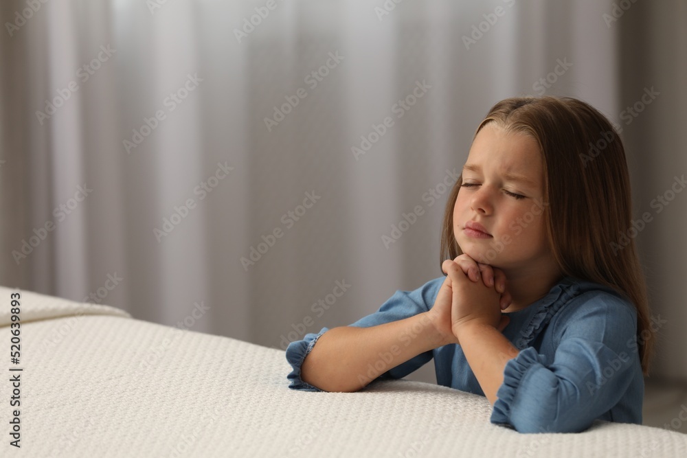 Cute little girl with hands clasped together saying bedtime prayer in bedroom. Space for text Cute little girl with hands clasped together saying bedtime prayer in bedroom. Space for text
