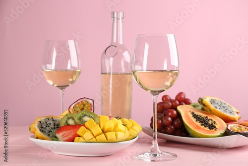Delicious exotic fruits and glasses of wine on pink wooden table