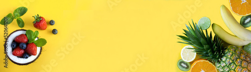 Banner. Tropical fruits and berry in half coconut on the yellow background. Close-up. Copy space.