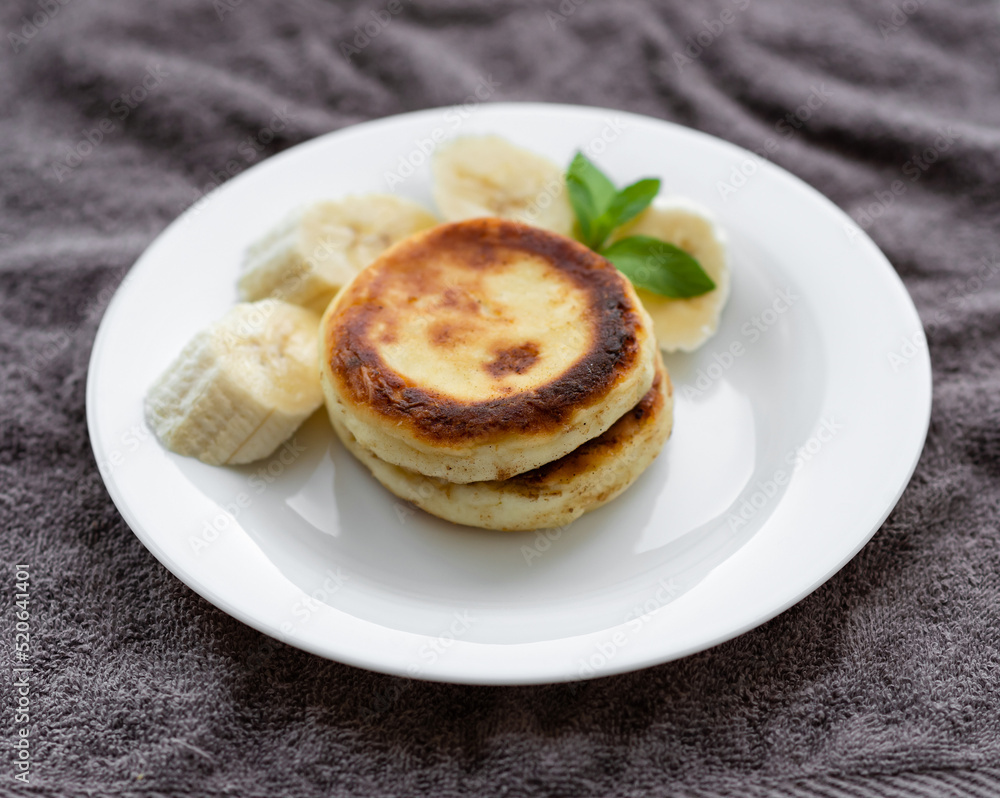 two curd fritters with sliced banana in a white plate