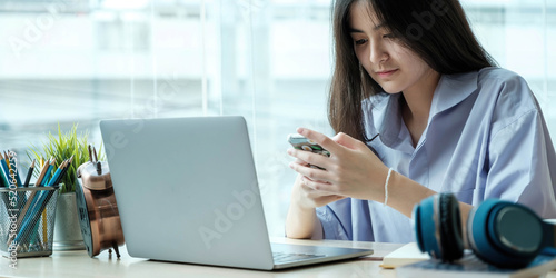 Female student taking notes from a book and using smart phone at home