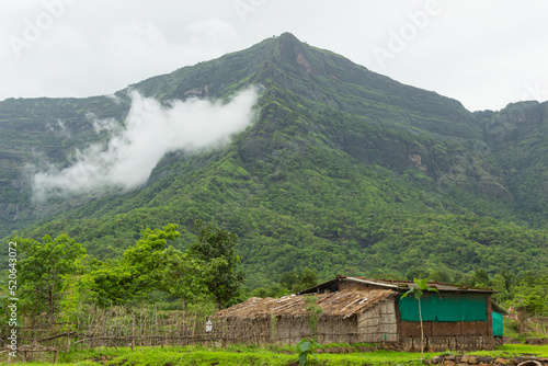 The Beautiful View of Sahyadri Mountain Range, Clouds Touching Hills and Hut Near The Hill,  photo