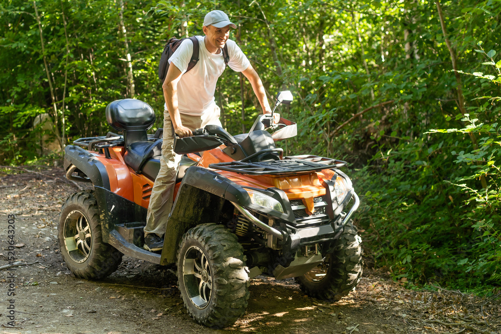 Fototapeta premium Young man driving off road adventure with happy and smiling. Man riding on ATV bike or quad bike on road along forest trail on mountain. Camping, jungle adventure concept.