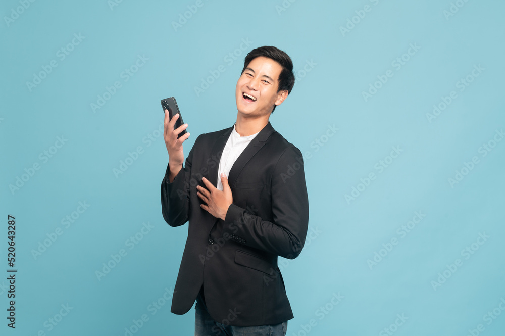 Young asian man in suit and jeans for smart casual business concept using smart phone isolated on blue background Young asian man in suit and jeans for smart casual business concept using smart phone isolated on blue background