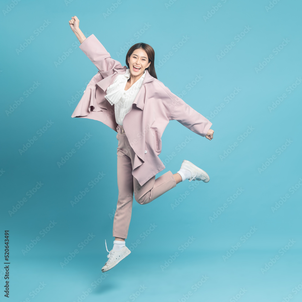 Young beautiful asian woman with smart casual cloth wearing pink coat jumping with excite feeling isolated on blue background Young beautiful asian woman with smart casual cloth wearing pink coat jumping with excite feeling isolated on blue background