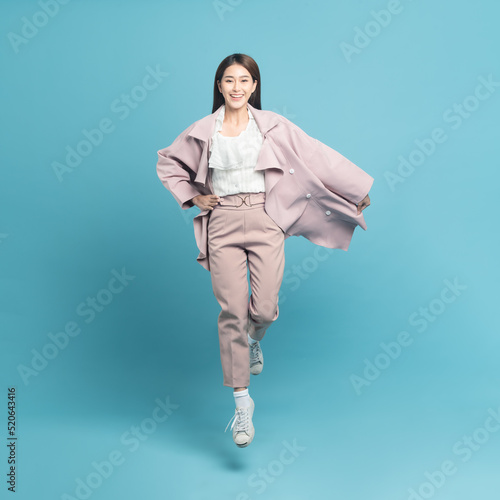 Young beautiful asian woman with smart casual cloth wearing pink coat smiling and jumping isolated on blue background
