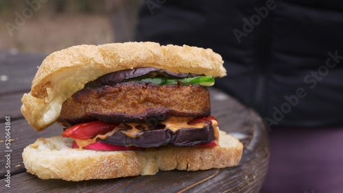 Delicious vegan burger made from plant-based meat substitute. Vegetables and a burger patty are grilled in the backyard. A juicy burger lies on a wooden table outside in the park.