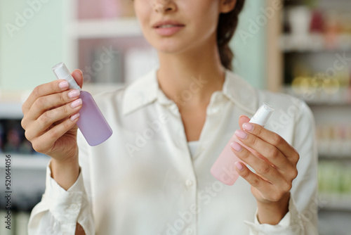 Hands of young shopper holding two plastic bottles with liquid nailcare products in cosmetic shop while deciding which one to choose photo