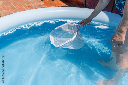 Woman cleaning her home's pool with a net, collecting leaves and trash to prevent infection.