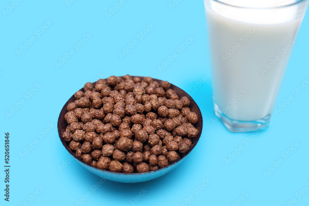 Corn chocolate flakes in the form of balls in a bowl and a glass of milk on a blue background. American style fast and healthy breakfast concept. Fast and easy energy food Corn chocolate flakes in the form of balls in a bowl and a glass of milk on a blue background. American style fast and healthy breakfast concept. Fast and easy energy food