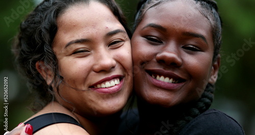 Two interracial girlfriends hugging each other, close-up interracial faces embrace © Marco
