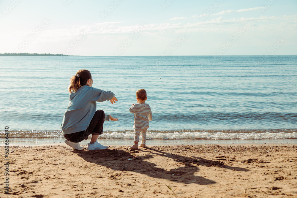 Mother teaches baby to throw stones in water sitting by the sea shore Mother teaches baby to throw stones in water sitting by the sea shore