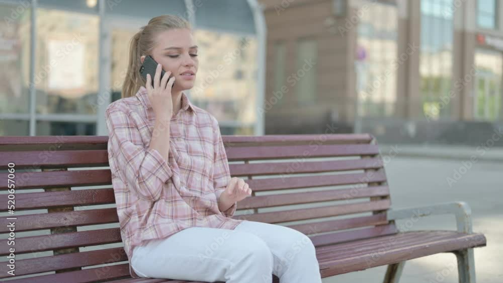 Young Woman Talking on Phone while Sitting Outdoor on Bench Young Woman Talking on Phone while Sitting Outdoor on Bench