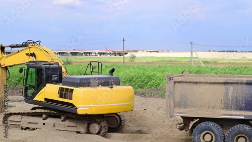 a yellow excavator performs leveling work on a road construction site and loads excess sand into a wheeled truck