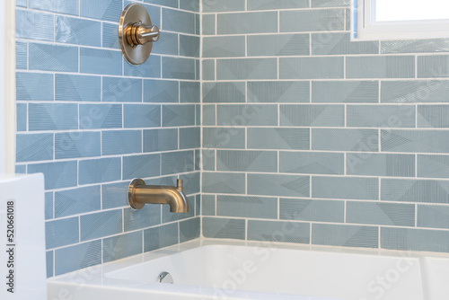 Light blue tile patterned bath tub tile with gold faucet and handle.