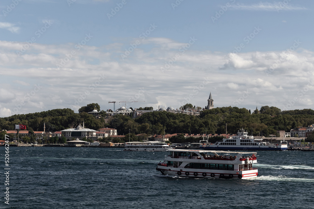 View of Bosphorus tour boats passing in front of Topkapi Palace in Istanbul. It is a sunny summer day.