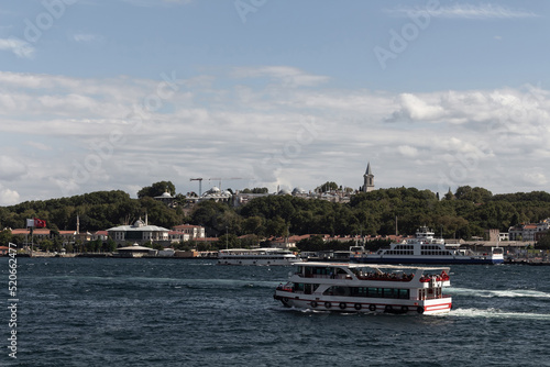 View of Bosphorus tour boats passing in front of Topkapi Palace in Istanbul. It is a sunny summer day.