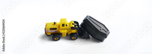 Toy yellow forklift with a coffin in a bucket on a white background. Concept of the exhumation of the coffin and forensic examination. Unusual game. Copy space.