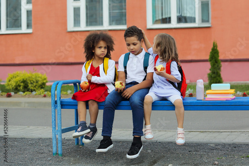 Cute Black schoolboy and girl are eating outdoors next the school. photo