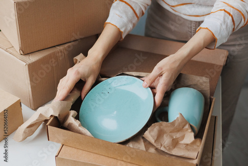 woman entrepreneur sells dishes, plates and cups made of clay, ceramics online and packs them in boxes for sending to the delivery service. small business selling goods on the Internet on the