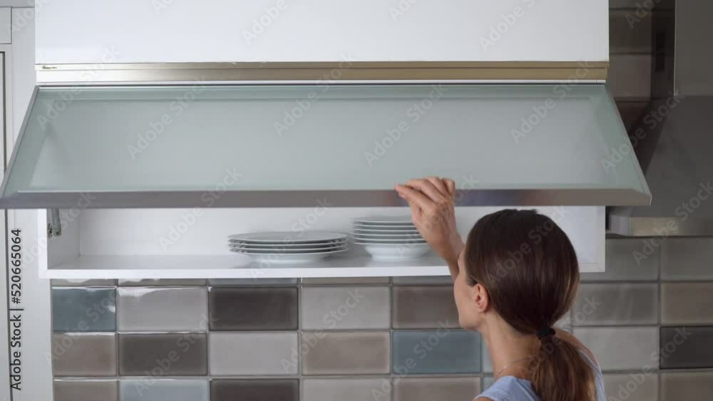 A woman opens a cupboard and takes a plate from the shelf A woman opens a cupboard and takes a plate from the shelf