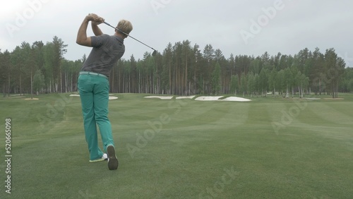 Golfer Hitting Ball with Club on Beautiful Golf Course. Golfer hits an fairway shot towards the club house. Man hitting driver on a golf course in the sun. Professional male golf player