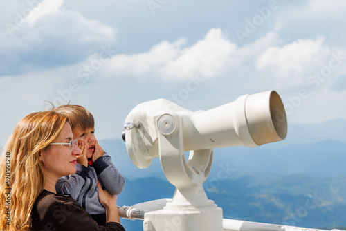 Mother shows son landscapes in valley of Rhodope Mountains and sky through telescope on observation tower of Snezhan