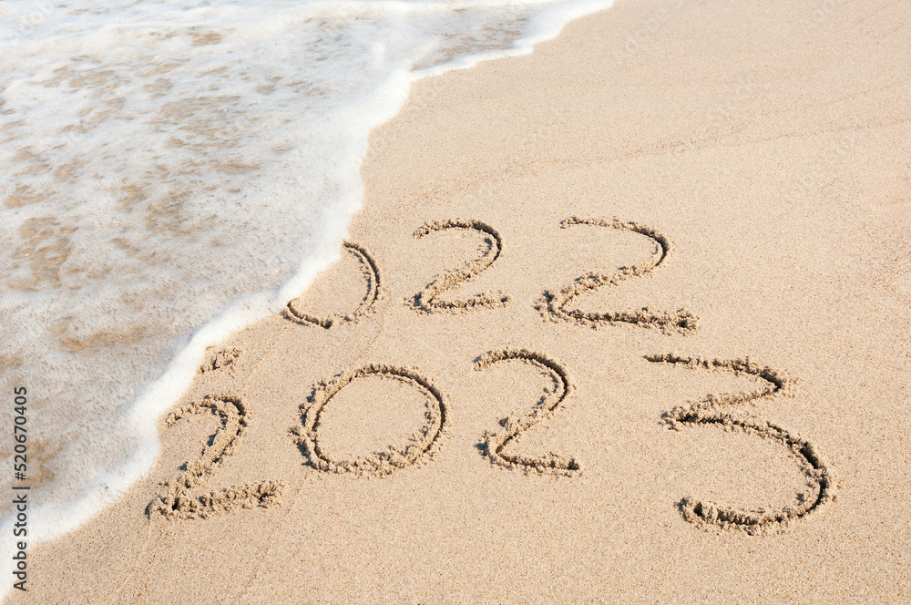 Inscription 2022 and 2023 numbers written on sand. New Year 2023