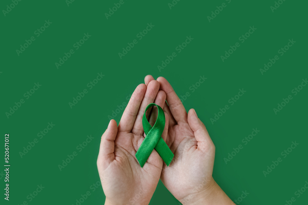 Adult hands holds green ribbon on green background. World lymphoma ...