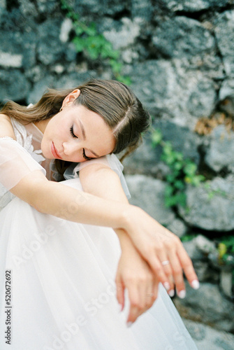 Bride in a white dress sits on stone steps with her head on her knees