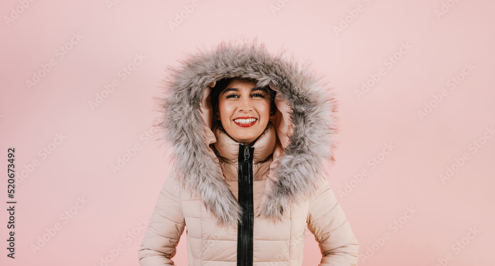 Portrait of young hispanic girl in winter coat smiling looking at camera on pink coral studio background in Mexico Latin America Portrait of young hispanic girl in winter coat smiling looking at camera on pink coral studio background in Mexico Latin America