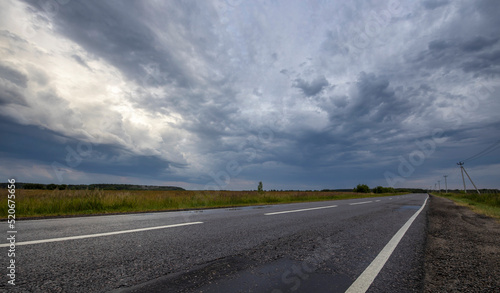 Dramatic sky over road and field. Evening rural landscape with thunderclouds.