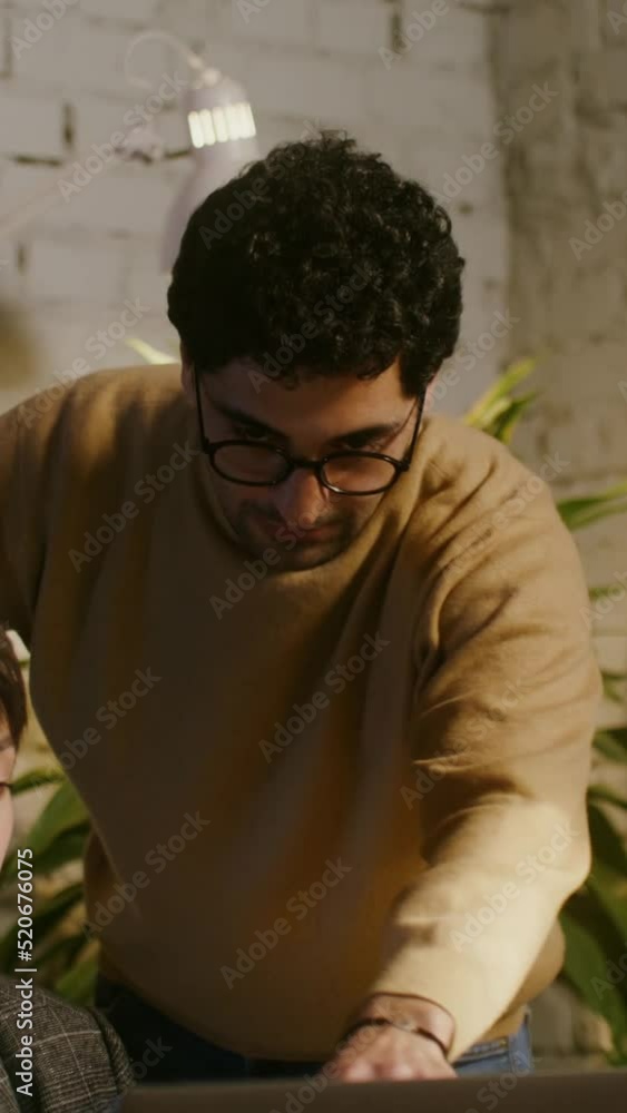A young man stands near a woman working on a laptop and shows into the screen A young man stands near a woman working on a laptop and shows into the screen
