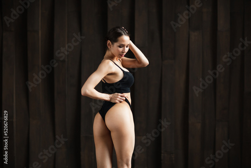 Beautiful sensual fitness woman with a good figure in black underwear, posing on dark