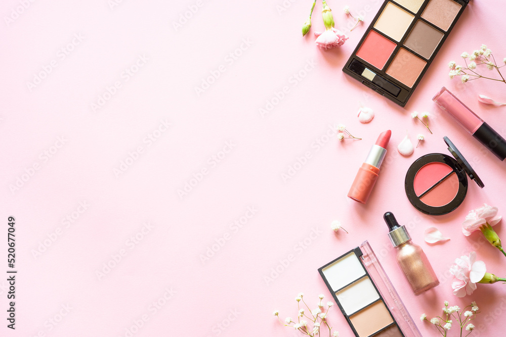 Makeup professional cosmetics on pink background with flowers. Flat lay with copy space.