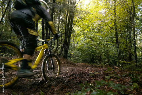 Cyclist in full face helmet on the yellow enduro bicycle fast rides in the mud in a green forest