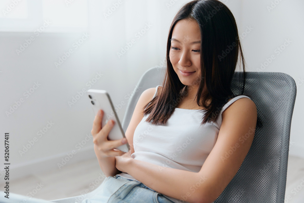 Cheerful lovely young Asian woman read cute messages from boyfriend in phone sit on chair at home interior living room. Distance communication Remote work Social media concept. Cool offer Banner Cheerful lovely young Asian woman read cute messages from boyfriend in phone sit on chair at home interior living room. Distance communication Remote work Social media concept. Cool offer Banner