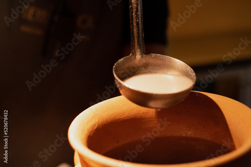 A spoon with warm and hot atole, chocolate, milk or cream, stirring in a brown pot at a Mexican traditional breakfast restaurant photo
