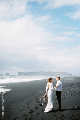 Bride and groom stand on the black Vik beach in Iceland