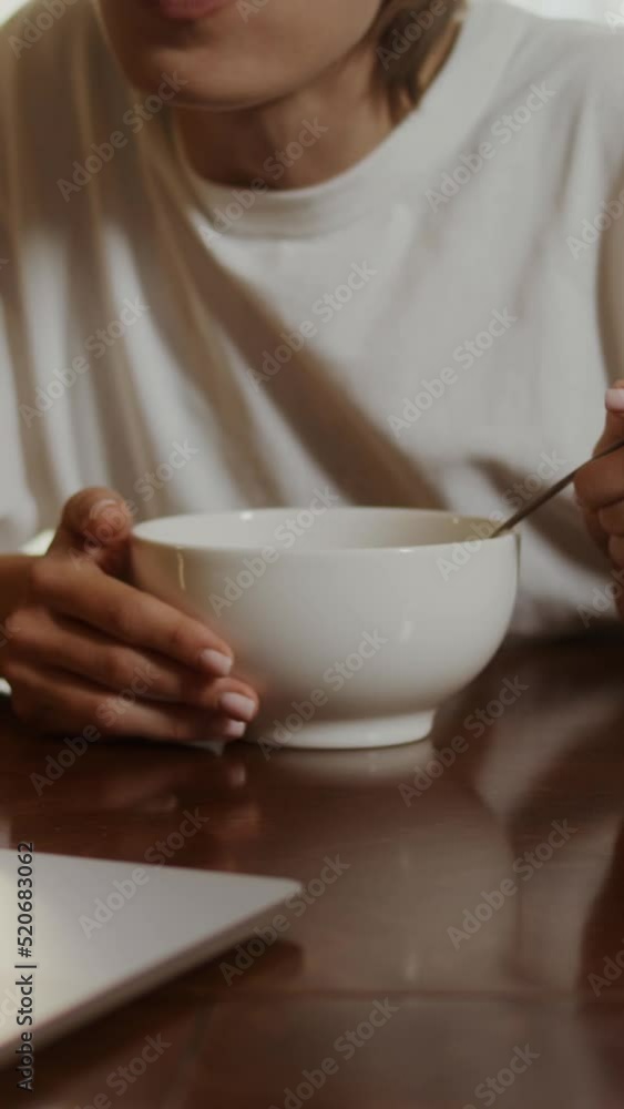 Young woman eats cereal with milk , sitting in front of a laptop Young woman eats cereal with milk , sitting in front of a laptop