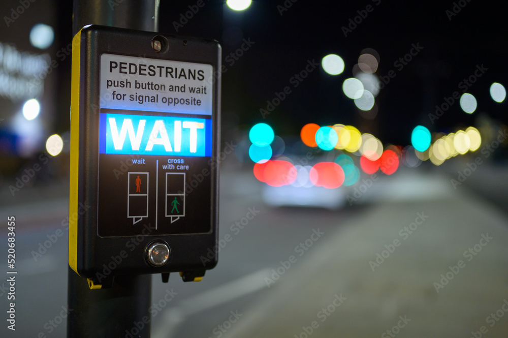 Pedestrian crossing button and illuminated wait sign with out of focus traffic in the background