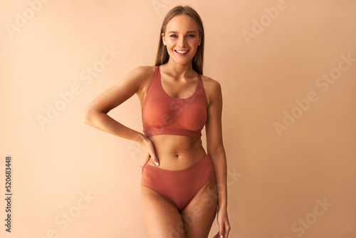 Attractive confident young woman posing on beige background in comfortable underwear and smiling.