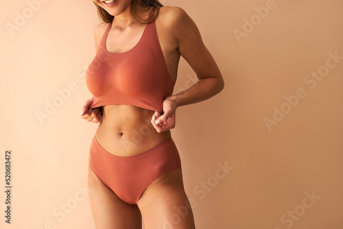   Cropped image of beautiful young woman posing in lingerie showing her bra on beige background.