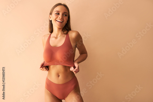 Portrait of a beautiful young woman posing in underwear showing her bra on a beige background.