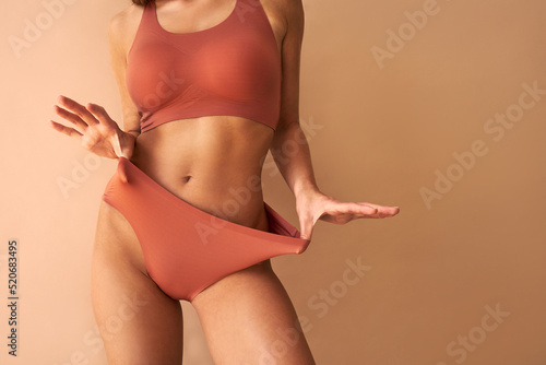 Cropped image of beautiful tanned young woman posing in comfortable underwear on beige background.Copy space.